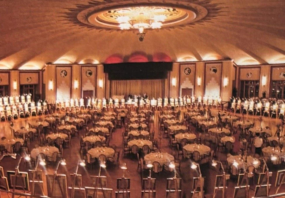 The Avalon Casino ballroom set with round dinner tables, ringed by easels displaying paintings